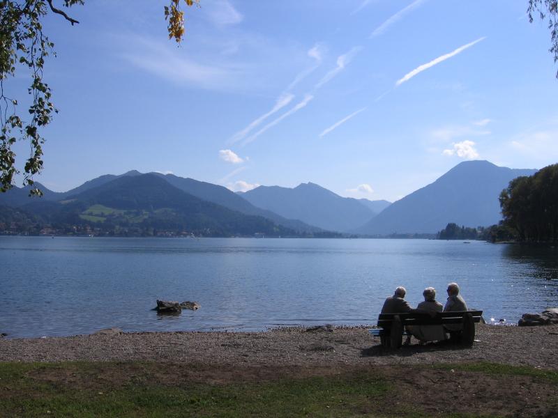 Tre persone sedute sulla riva del lago davanti a un paesaggio montano