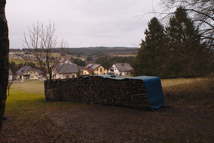 Vista su Neuhütten da un sentiero verso il Dollberg con catasta di legna in primo piano