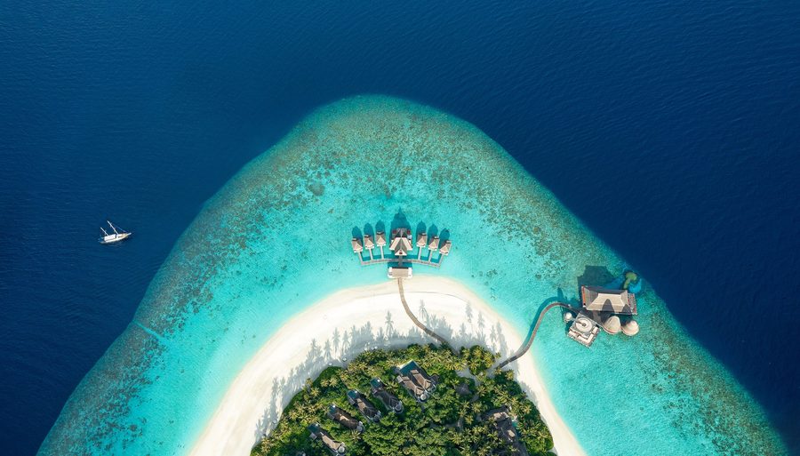 Aerial view of a Maldives resort island surrounded by a turquoise lagoon and reef.