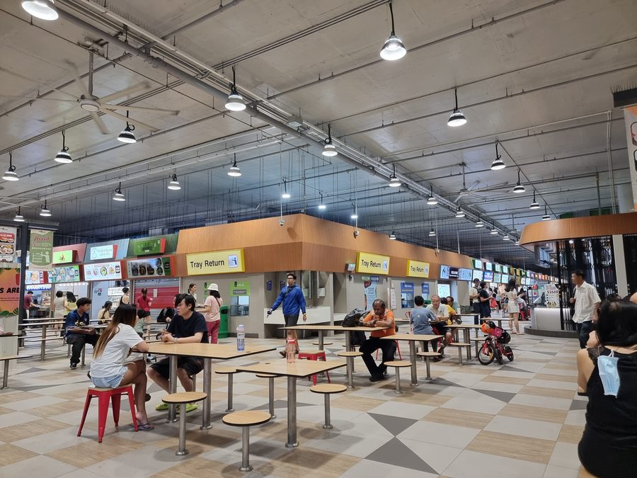 Interno del Woodleigh Village Hawker Centre con diversi stand gastronomici